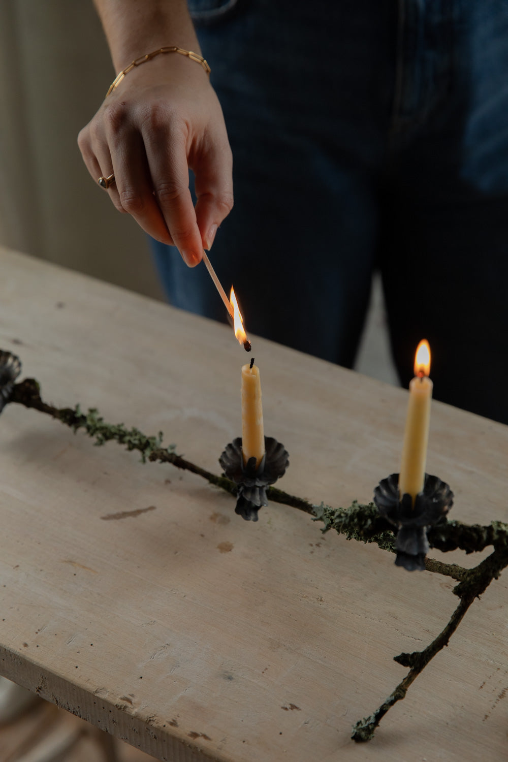 Person lighting two candles on a decorative branch with a blurred background