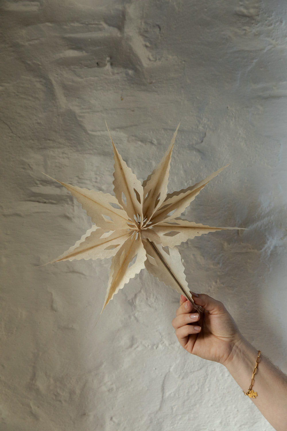 Hand holding a star-shaped object against a textured beige wall