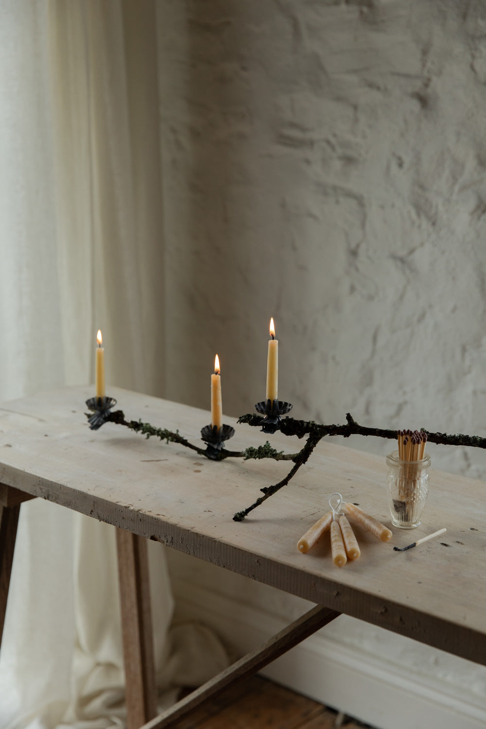 Candle holder with lit candles on a wooden table against a textured wall.