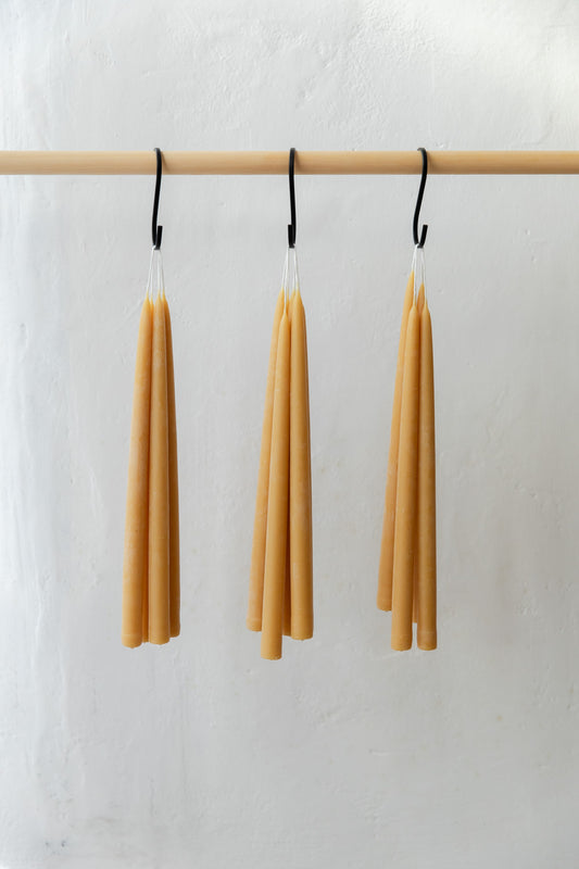 Three hanging bundles of beeswax candles on a wooden rod against a white background