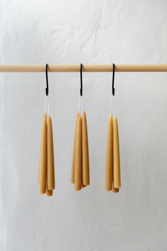 Three bundles of beeswax candles hanging from a wooden rod against a white background