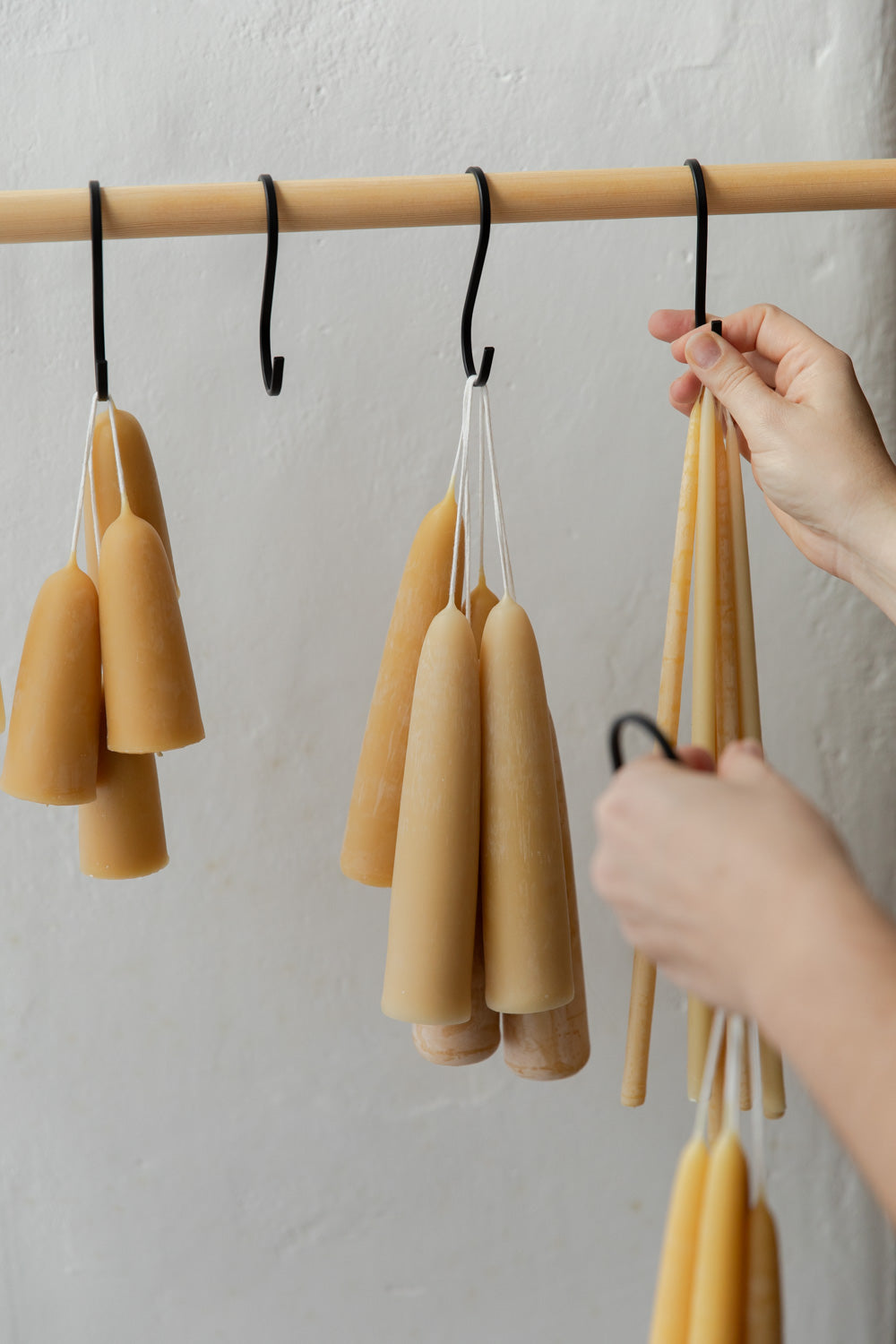 Beeswax candles hanging on a wooden rod against a white wall.