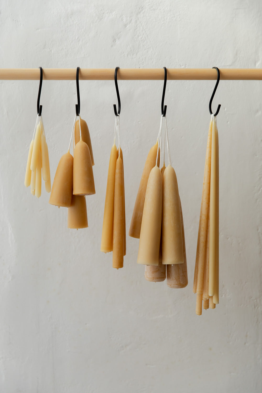 Beeswax candles hanging from a wooden rod against a light gray background