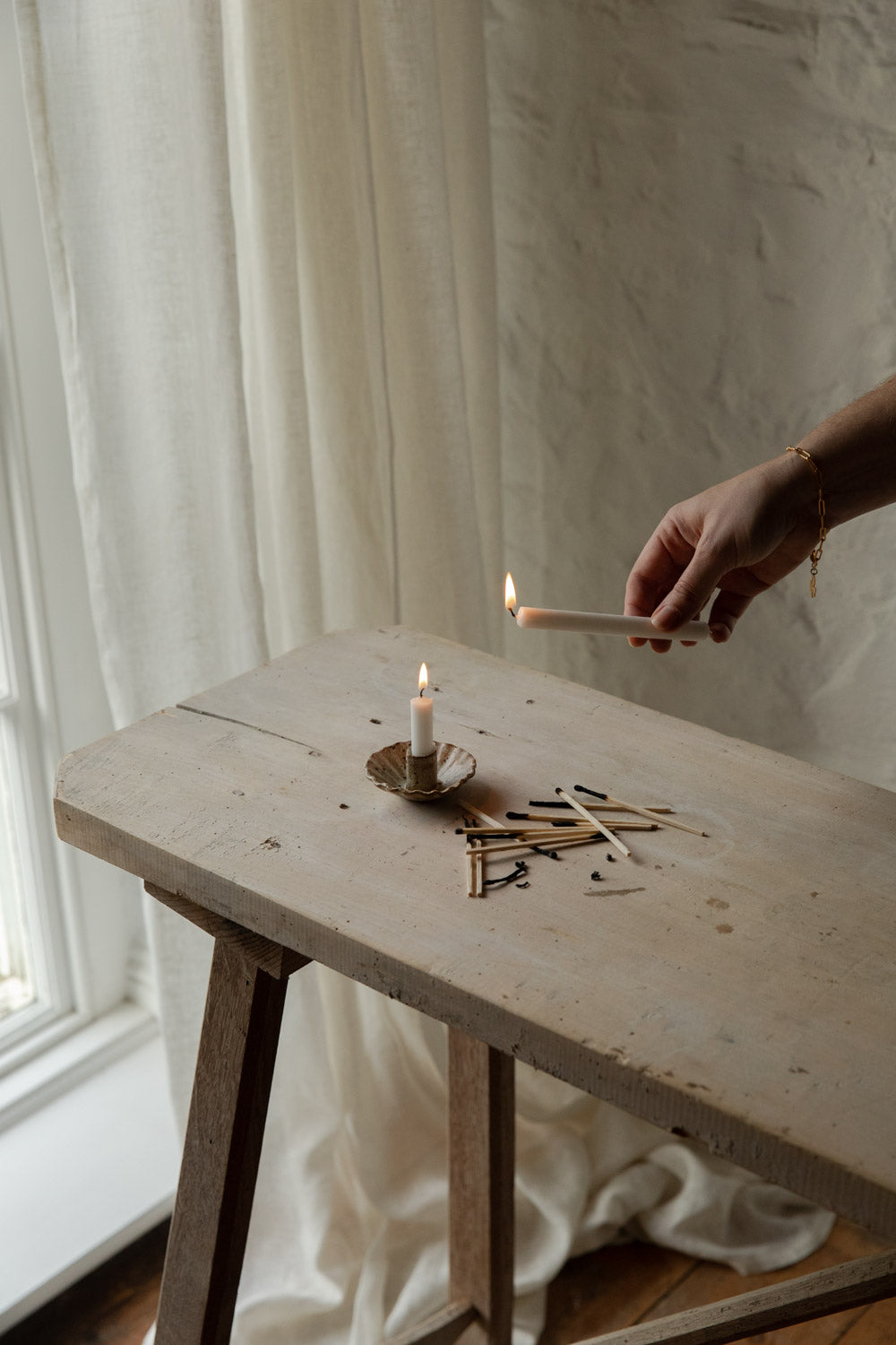 Person lighting a candle on a wooden table with a soft, neutral background
