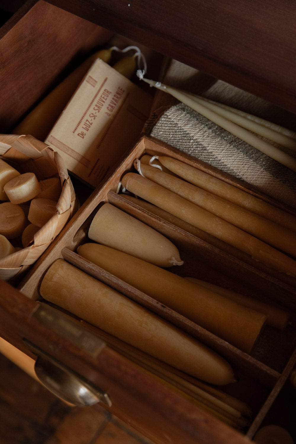 Wooden drawer full of beeswax candles of all different sizes.