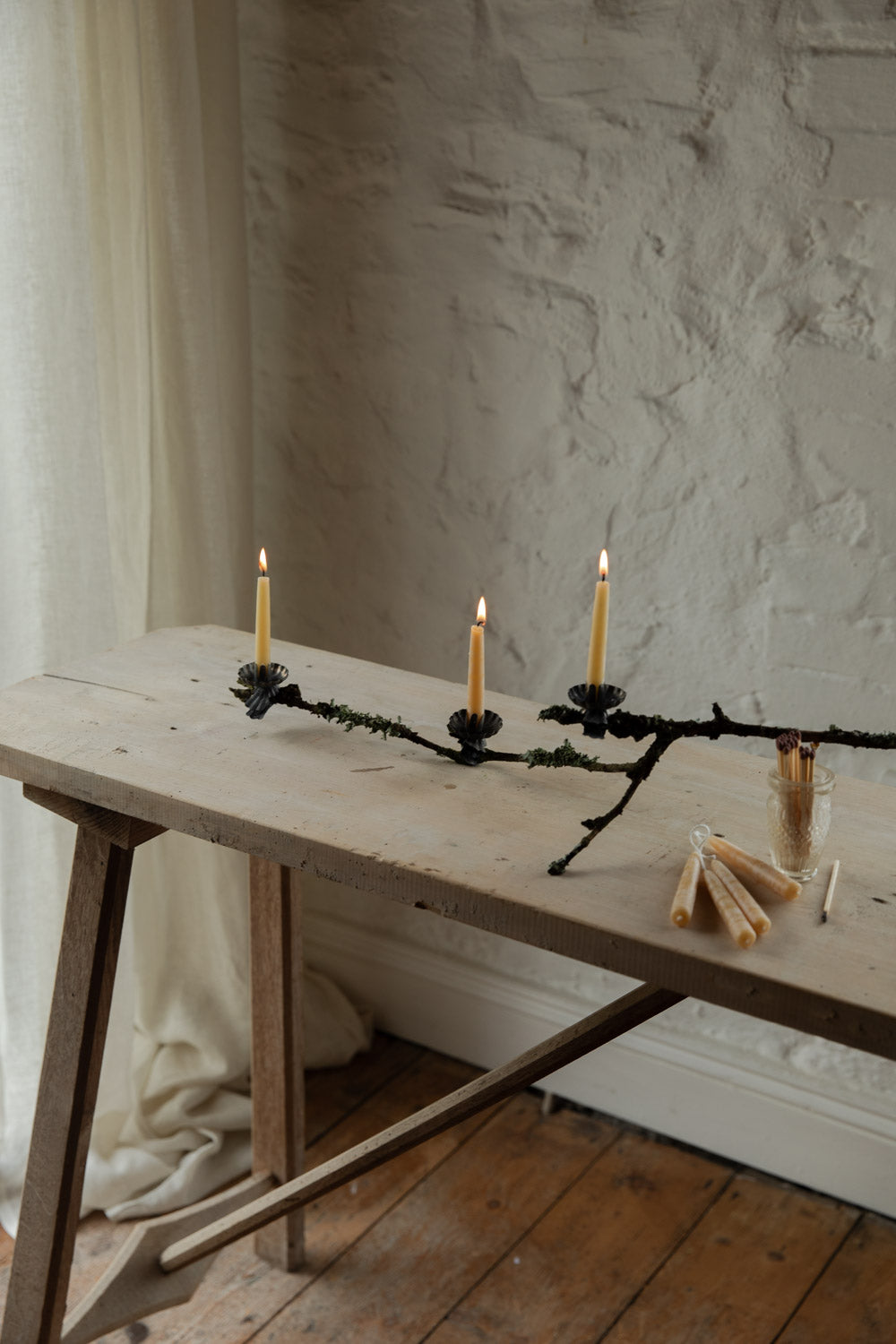 Wooden table with candles and branches against a textured wall.