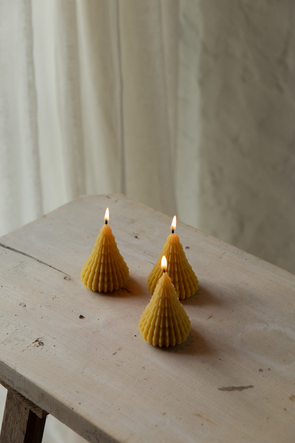 Three beeswax tree shaped candles on a wooden surface with a neutral background