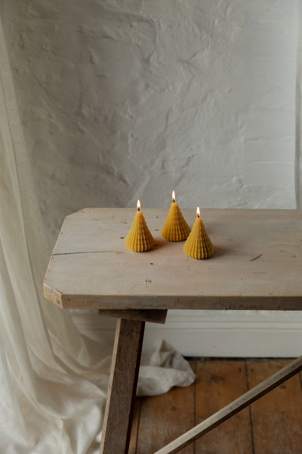 Three tree-shaped candles on a wooden table against a white wall.
