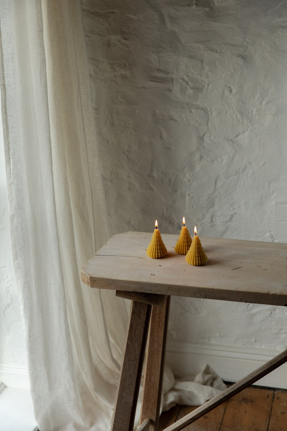 Three small candles on a wooden table against a textured wall.