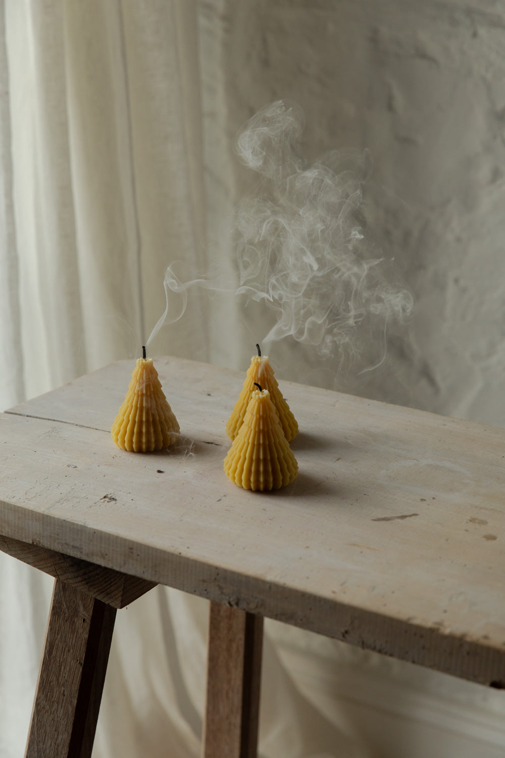 Three cone-shaped candles emitting smoke on a wooden surface with a white curtain background.