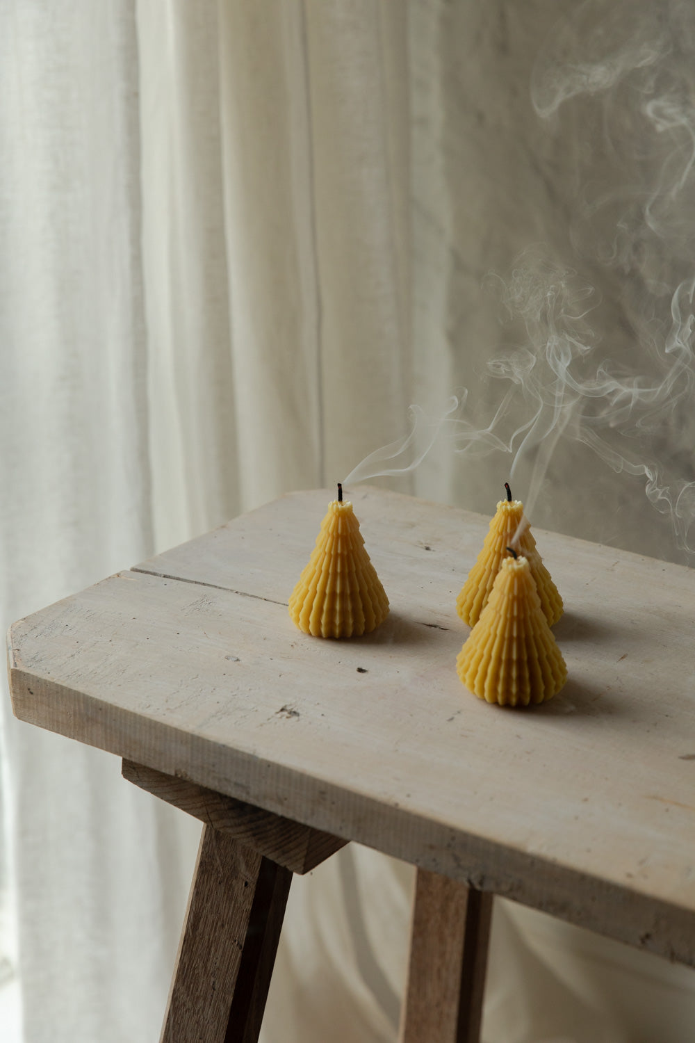 Three beeswax textured candles on a wooden table with a light background