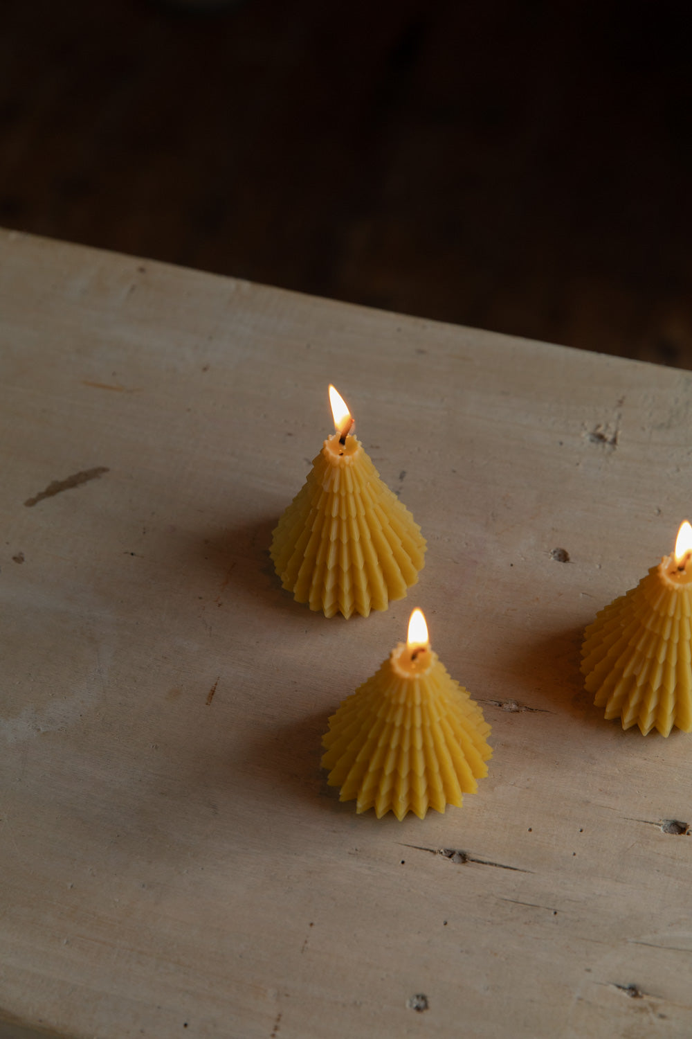 Three beeswax candles with textured bases on a wooden surface.