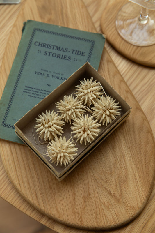 Decorative items in a box on a wooden surface with a book titled 'Christmas Tide Stories' in the background.