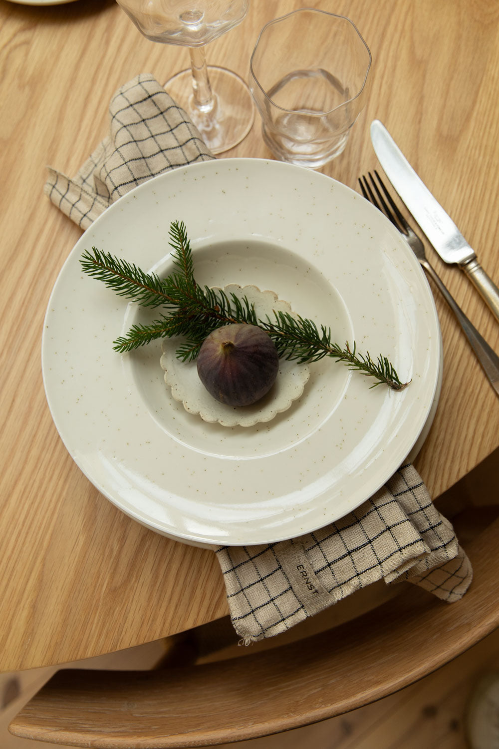 Dinner setting with a white plate featuring a fig and sprig of rosemary, on a wooden table.