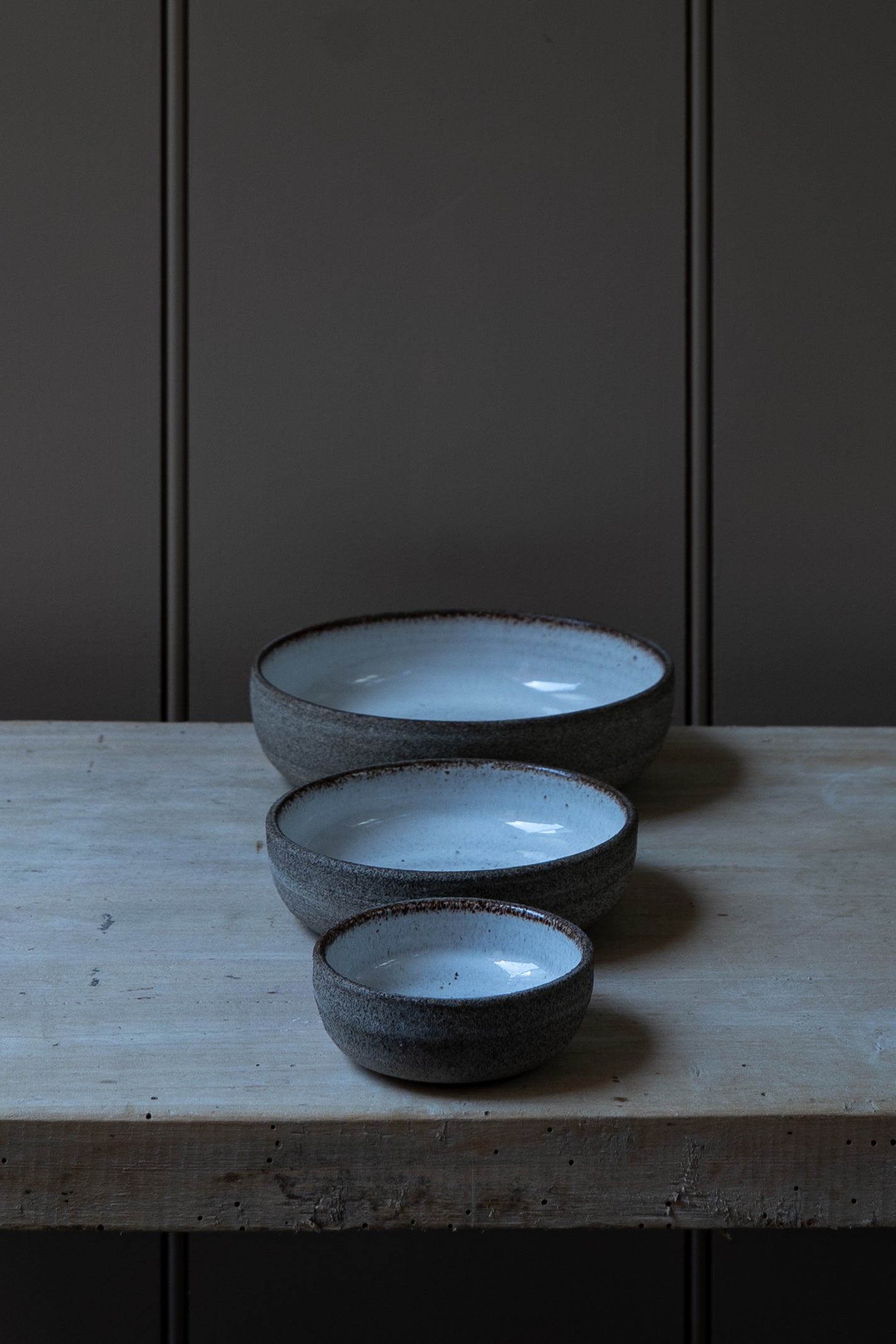 Three ceramic bowls of varying sizes on a wooden surface with a dark background