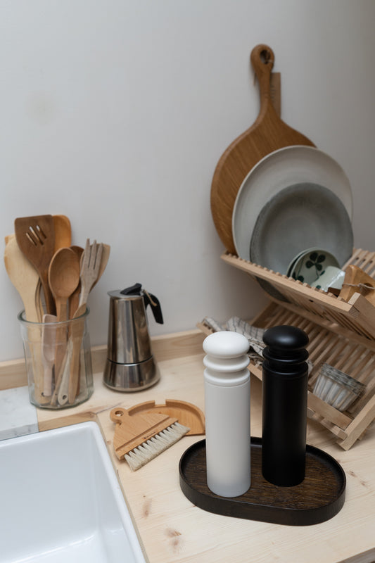 Kitchen counter with wooden utensils, a coffee press, wooden black and white pepper mill and a dish rack.