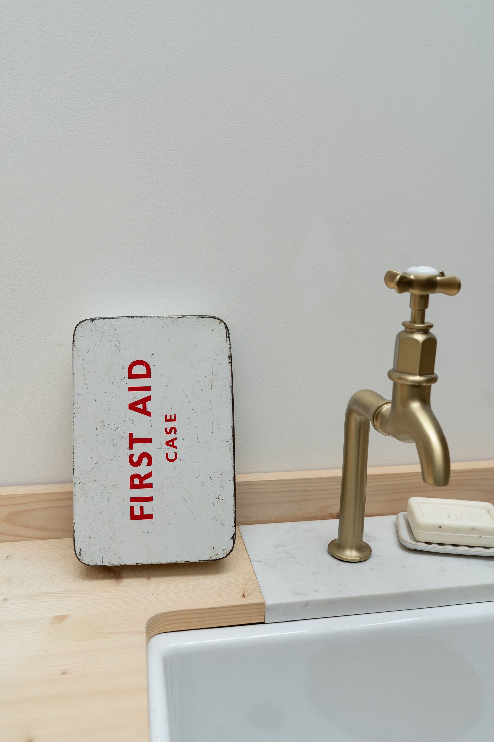 Small metal first aid case on a sink counter with a gold faucet in the background.