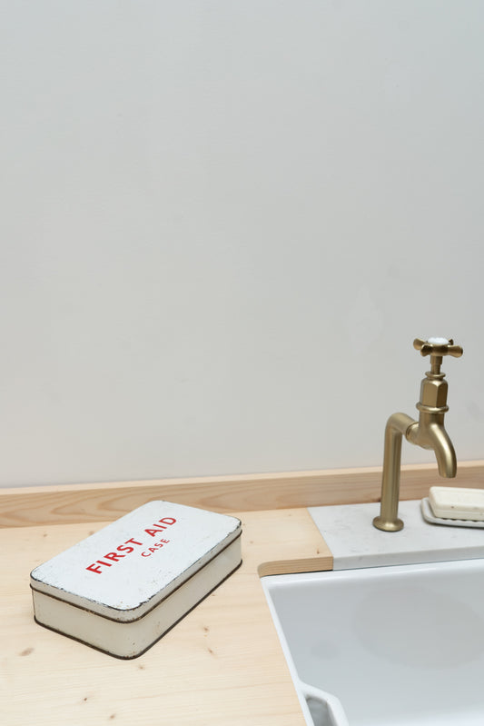 First aid kit on a wooden surface next to a sink with a gold faucet.