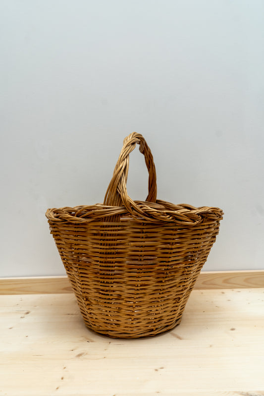 Wicker basket with handle on a wooden floor against a light gray wall