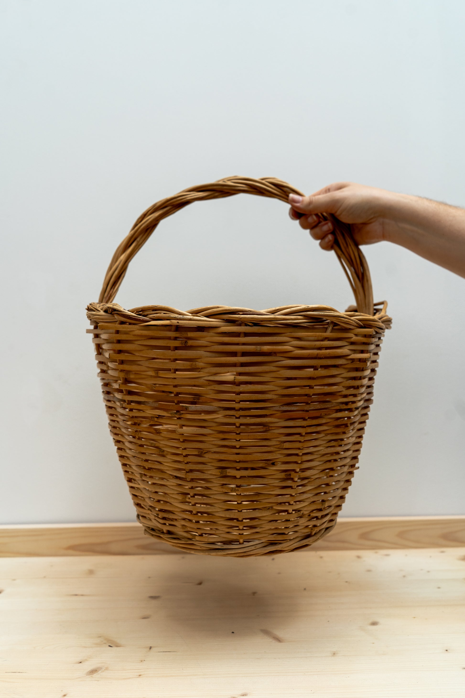 Hand holding a woven basket on a wooden surface with a white background