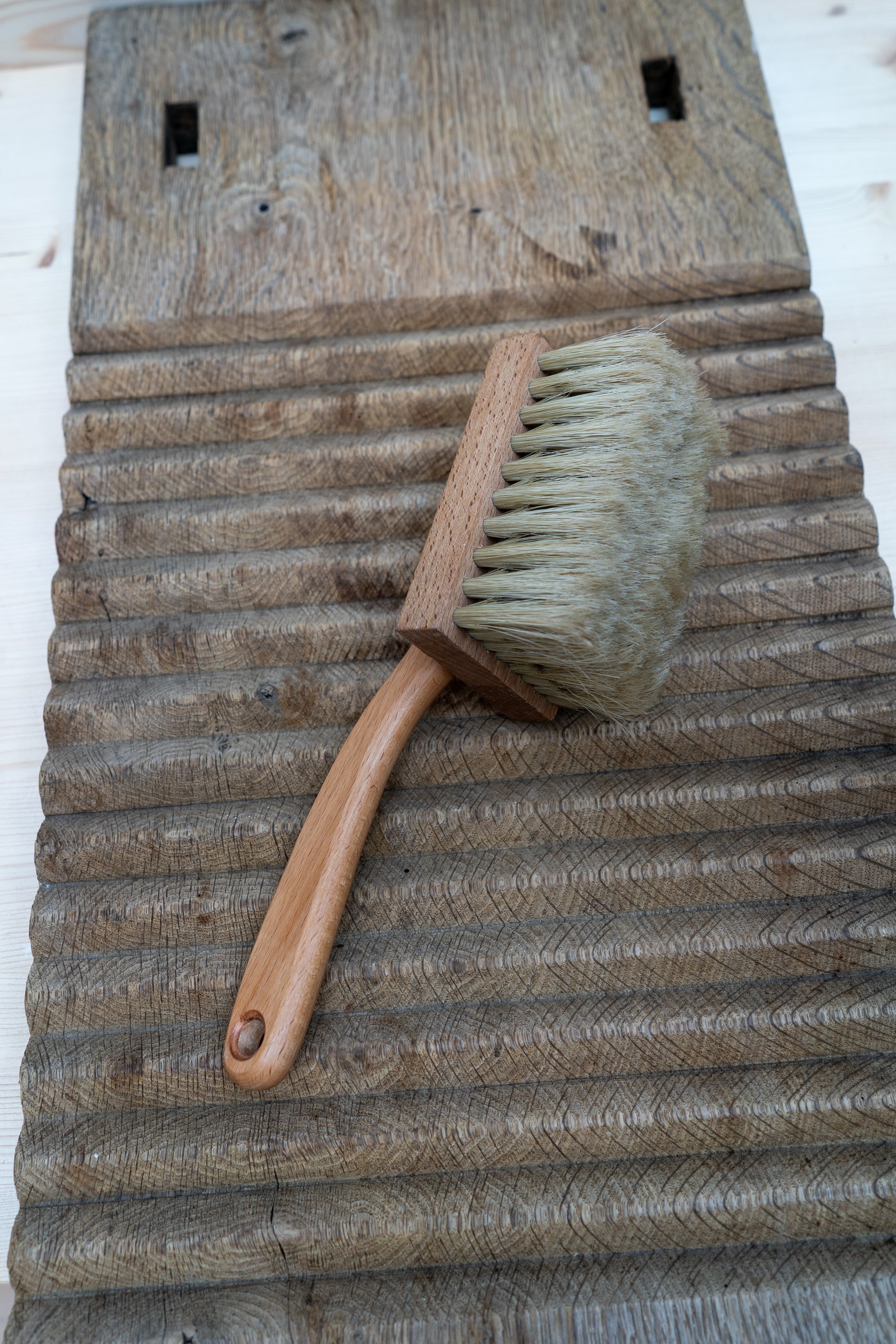 Handheld brush with wooden handle and bristle head on a rustic wooden surface
