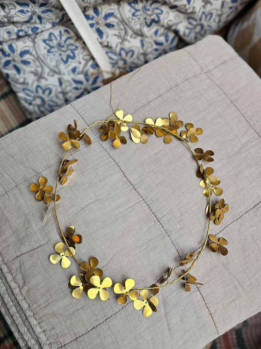 Brass Clover wreath on a folded beige quilt.