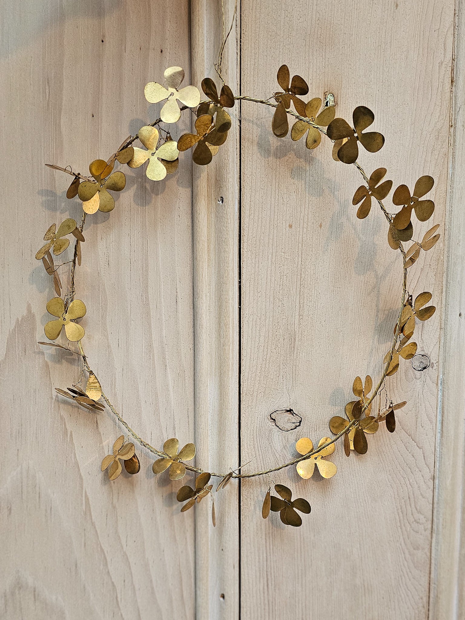 Brass Clover wreath hanging in front of old wooden door.