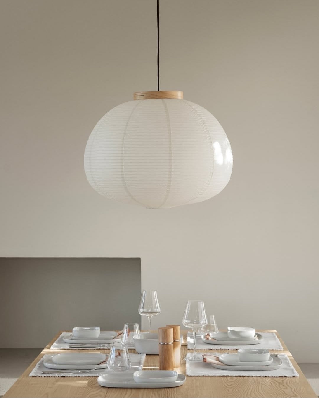 Modern pendant light hanging above a dining table with white plates and glasses.