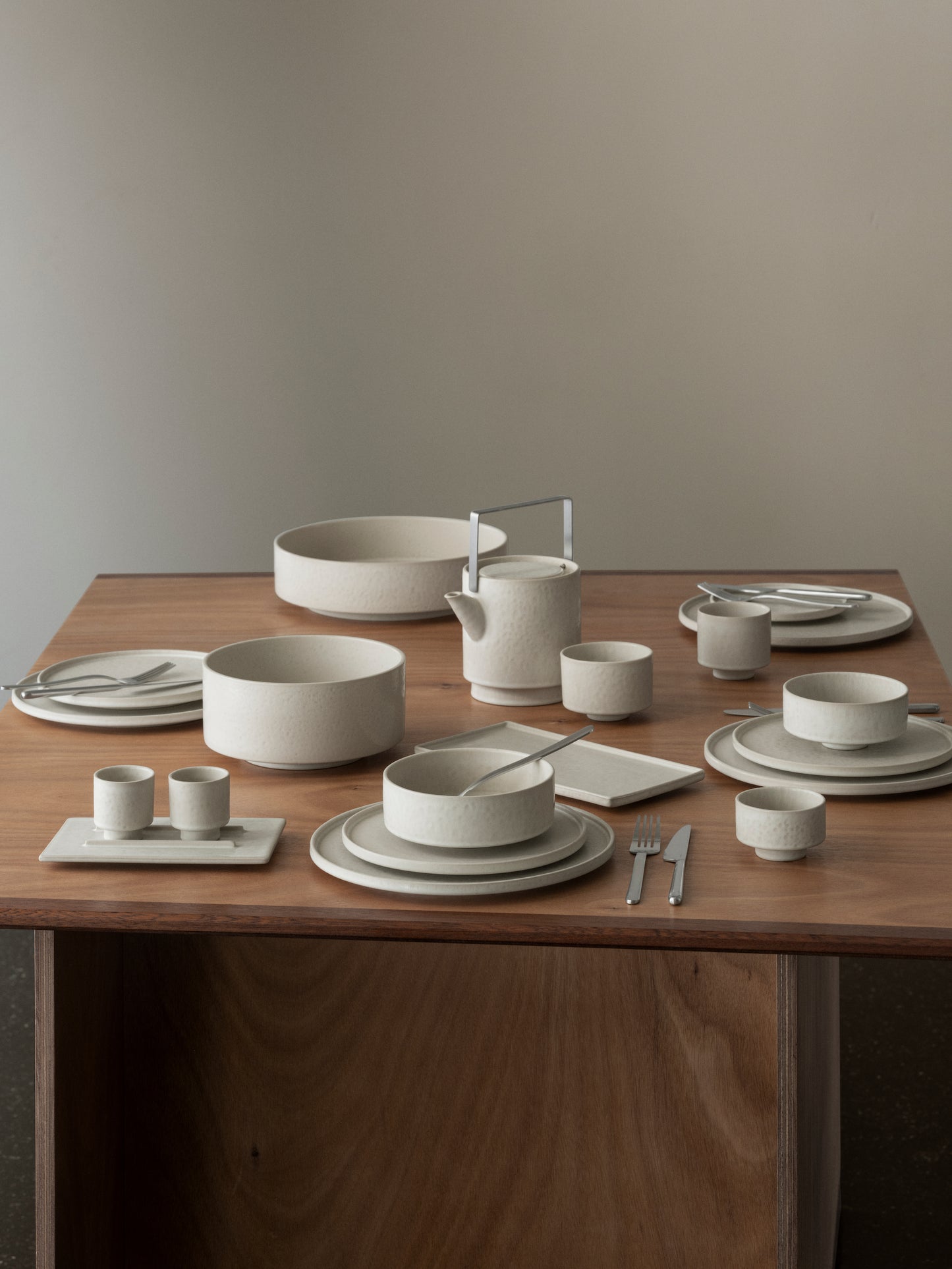 Dining table set with ceramic dishes and cutlery on a wooden surface.