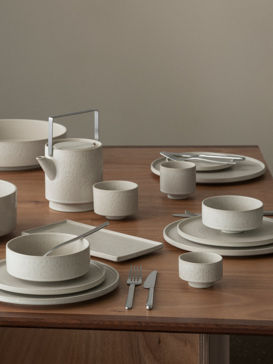 Set of ceramic tableware including bowls, cups, and a teapot on a wooden table.