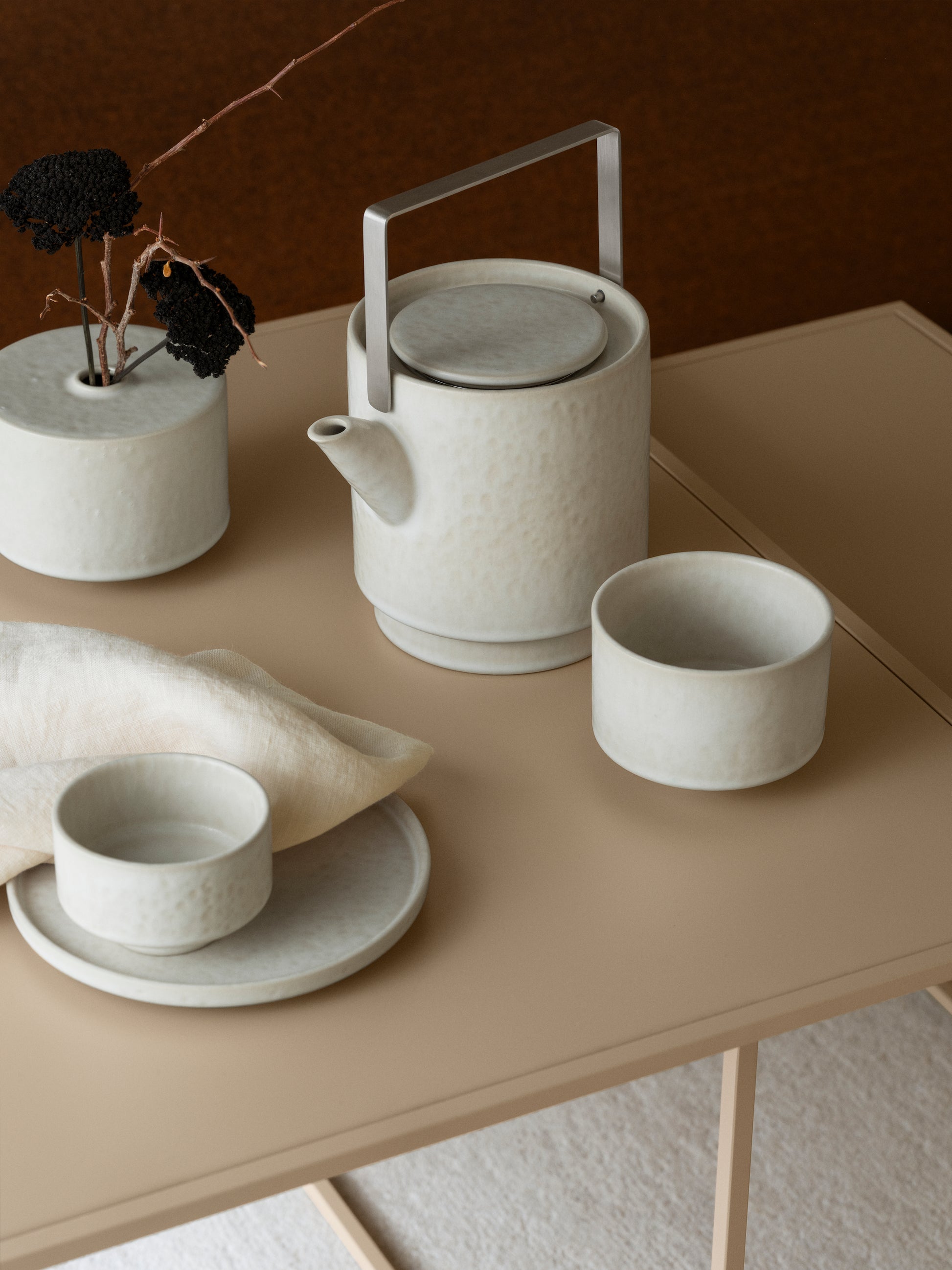Ceramic tea pot, vase and cups on a beige table with a brown background