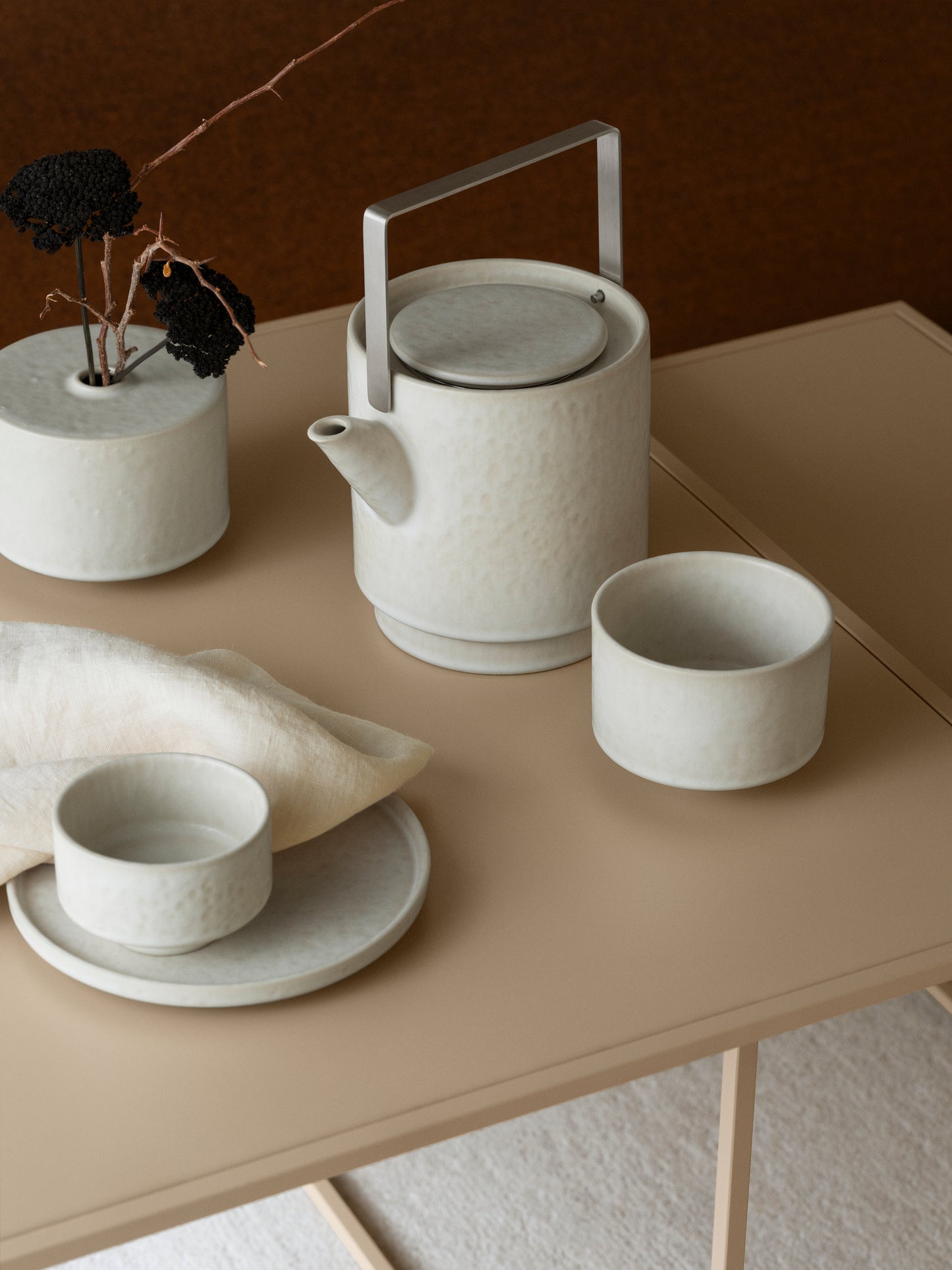 Ceramic tea pot, vase and cups on a beige table with a brown background