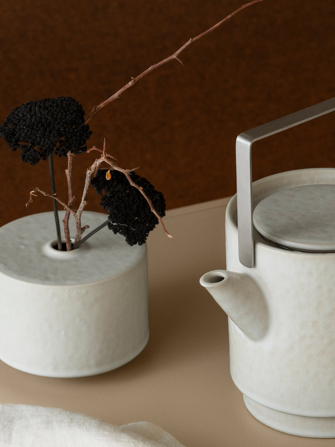 White ceramic teapot and small vase with black flowers on a brown background