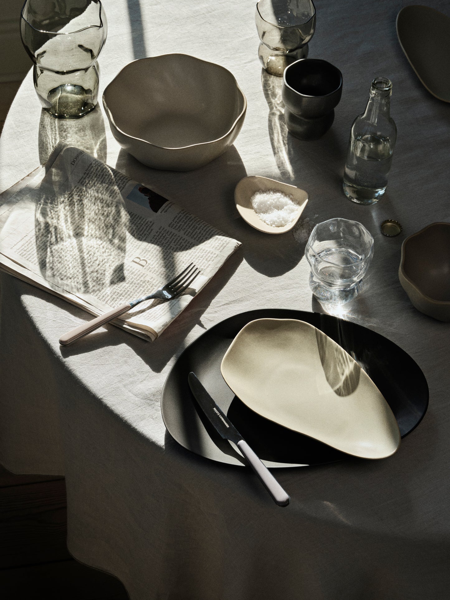Dining table setting with modern ceramic plates, bowls, and cutlery on a textured surface.