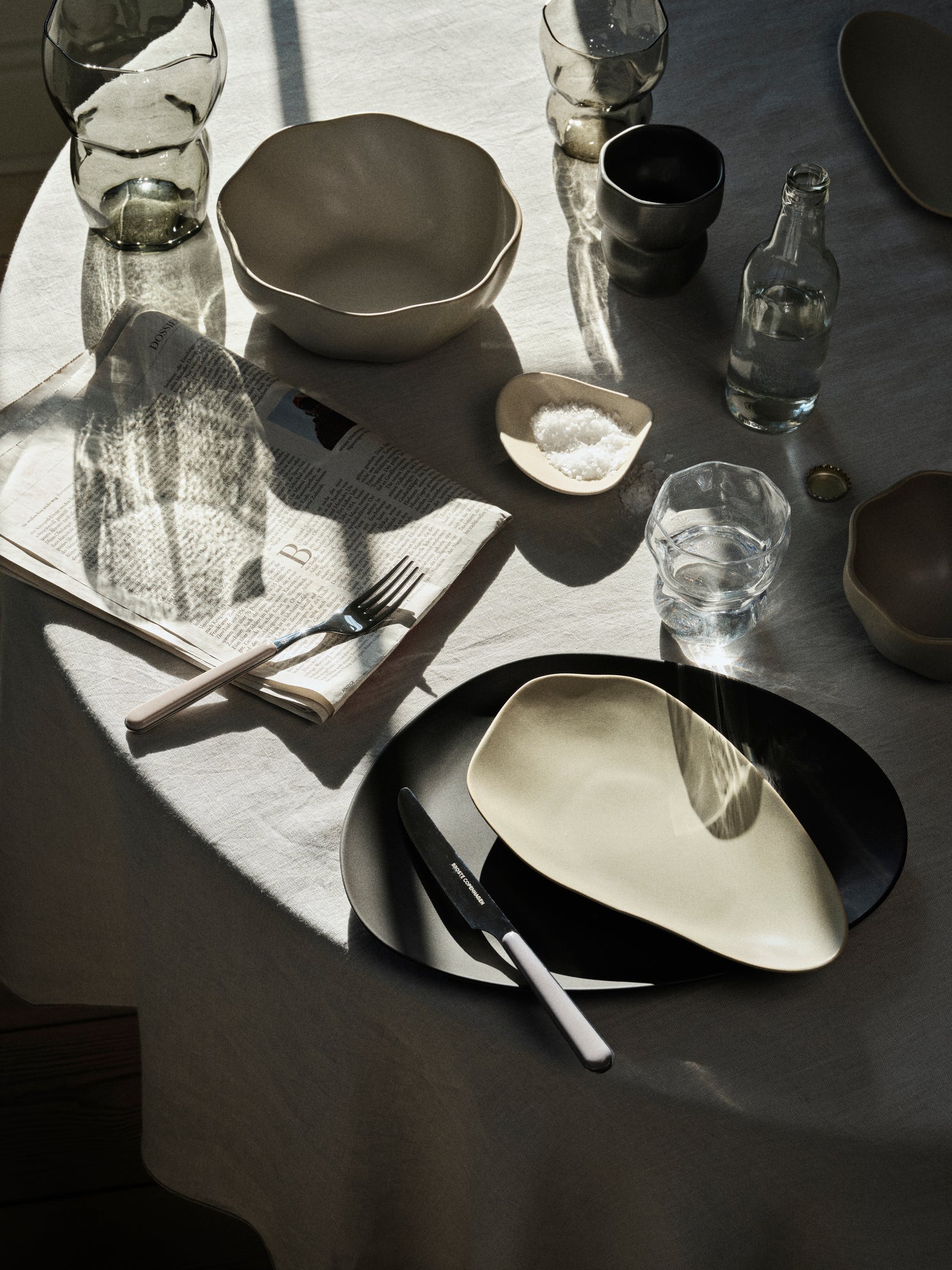 Dining table setting with modern ceramic plates, bowls, and cutlery on a textured surface.