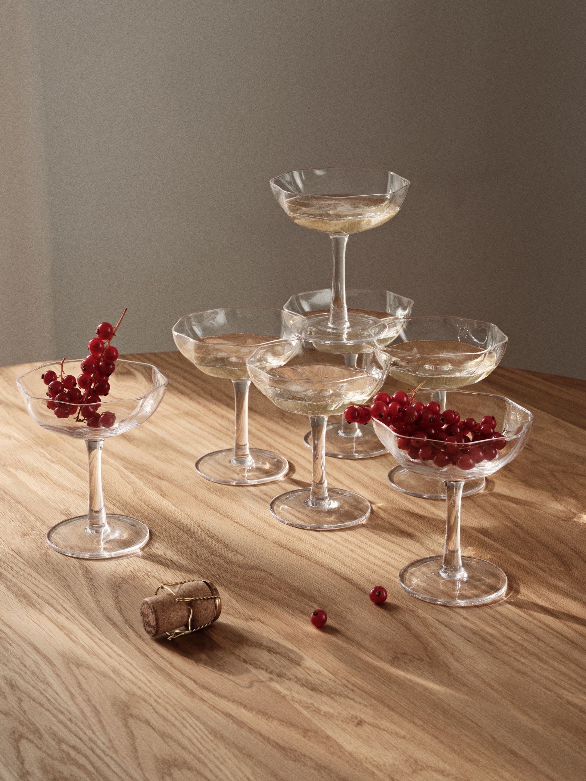 Set of clear glass cocktail glasses with red berries on a wooden surface