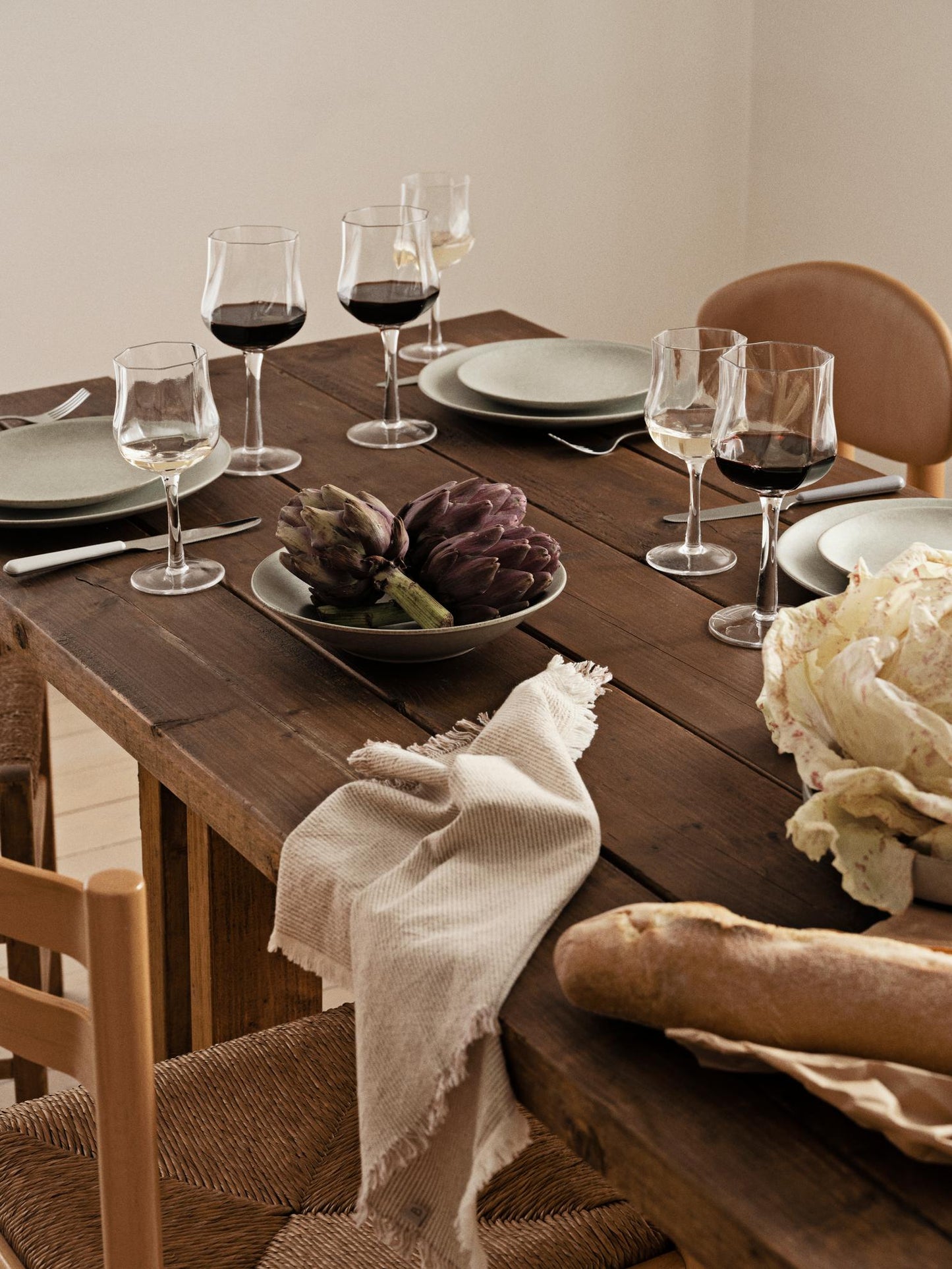 Dining table set with wine glasses, plates, and bread on a wooden table.