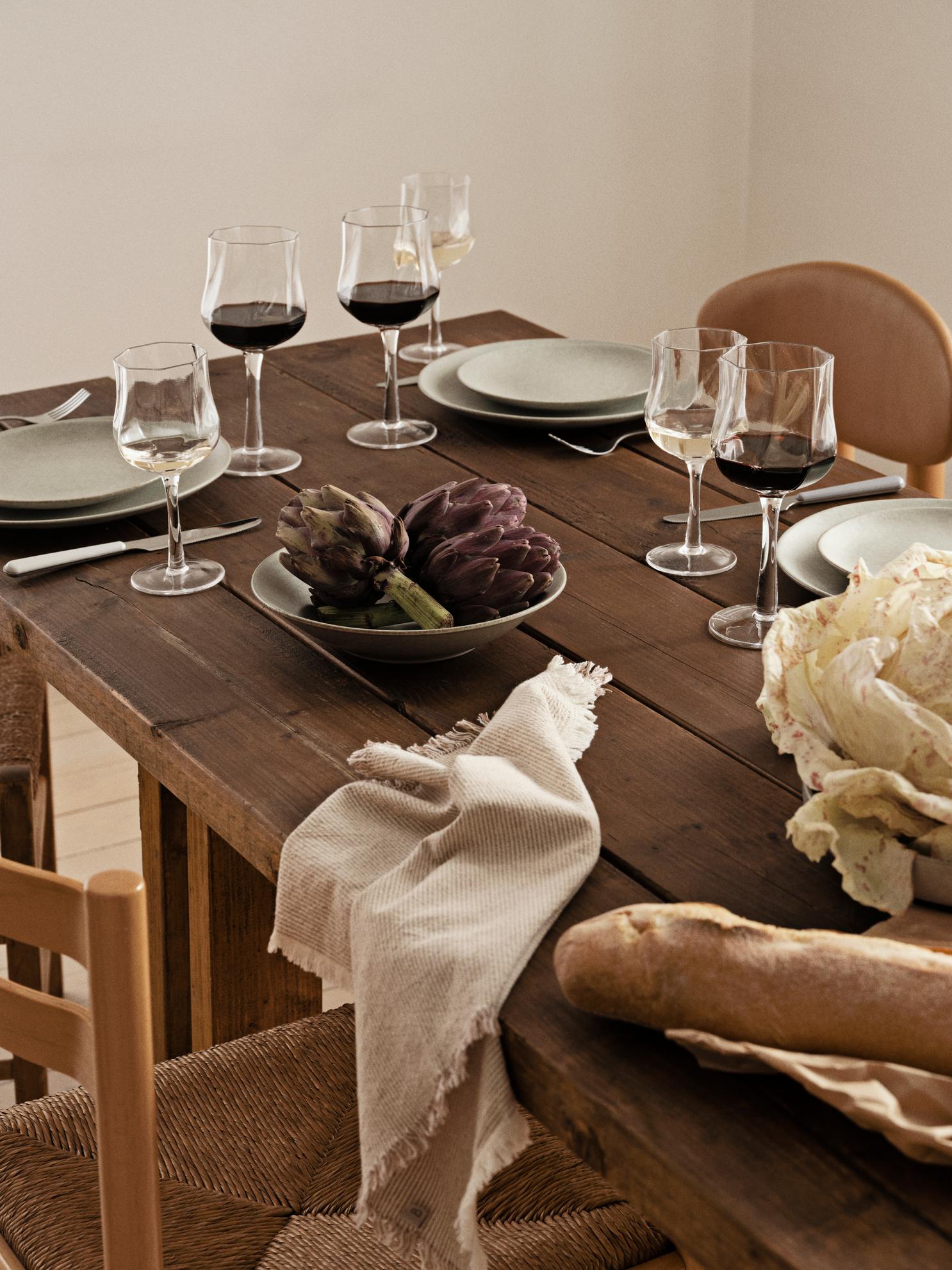 Dining table set with wine glasses, plates, and bread on a wooden table.