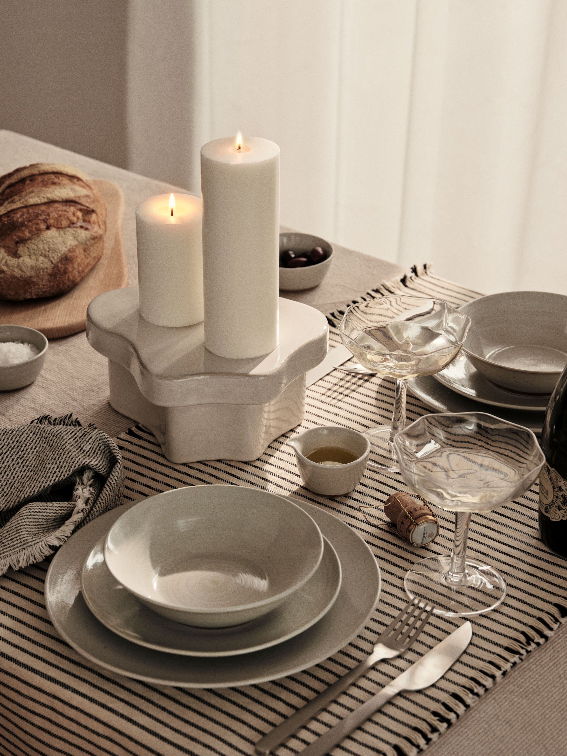 Dining table setting with white candles, plates, and glasses on a striped tablecloth.