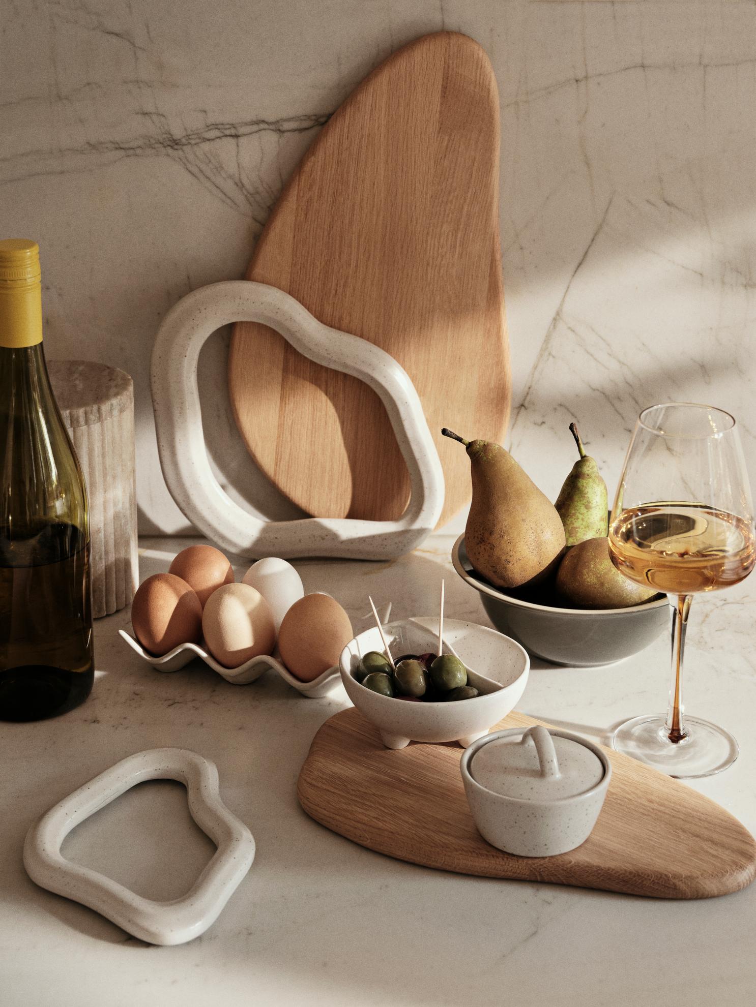 Table setting with wooden and ceramic items including a bottle, eggs, pears, and a glass of wine.