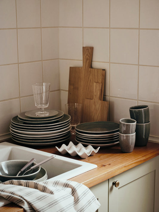 Kitchen counter with dishes, glasses, and cutting boards against a tiled wall.