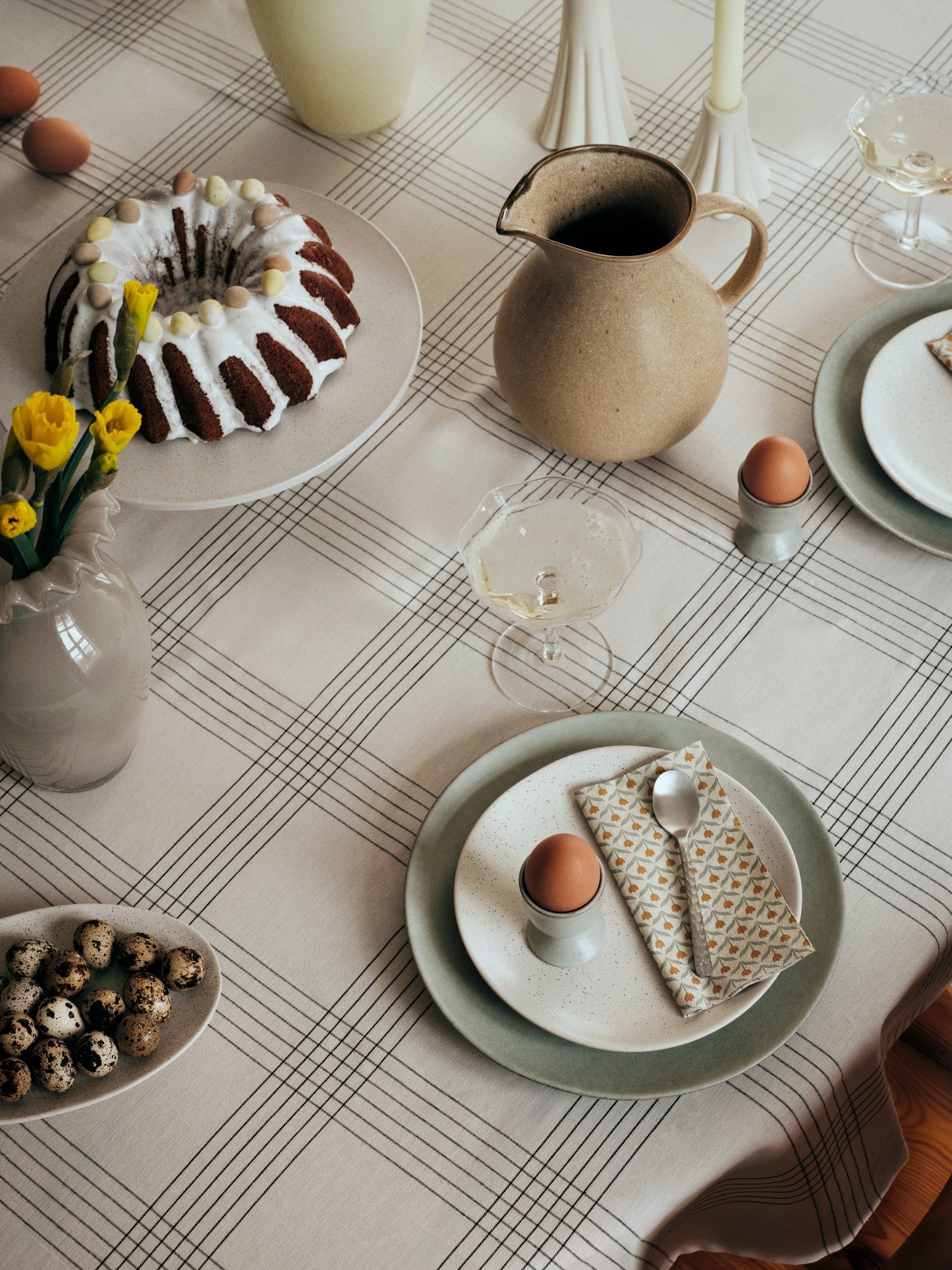 Easter table setting with cake, eggs, and decorative items on a checkered tablecloth.