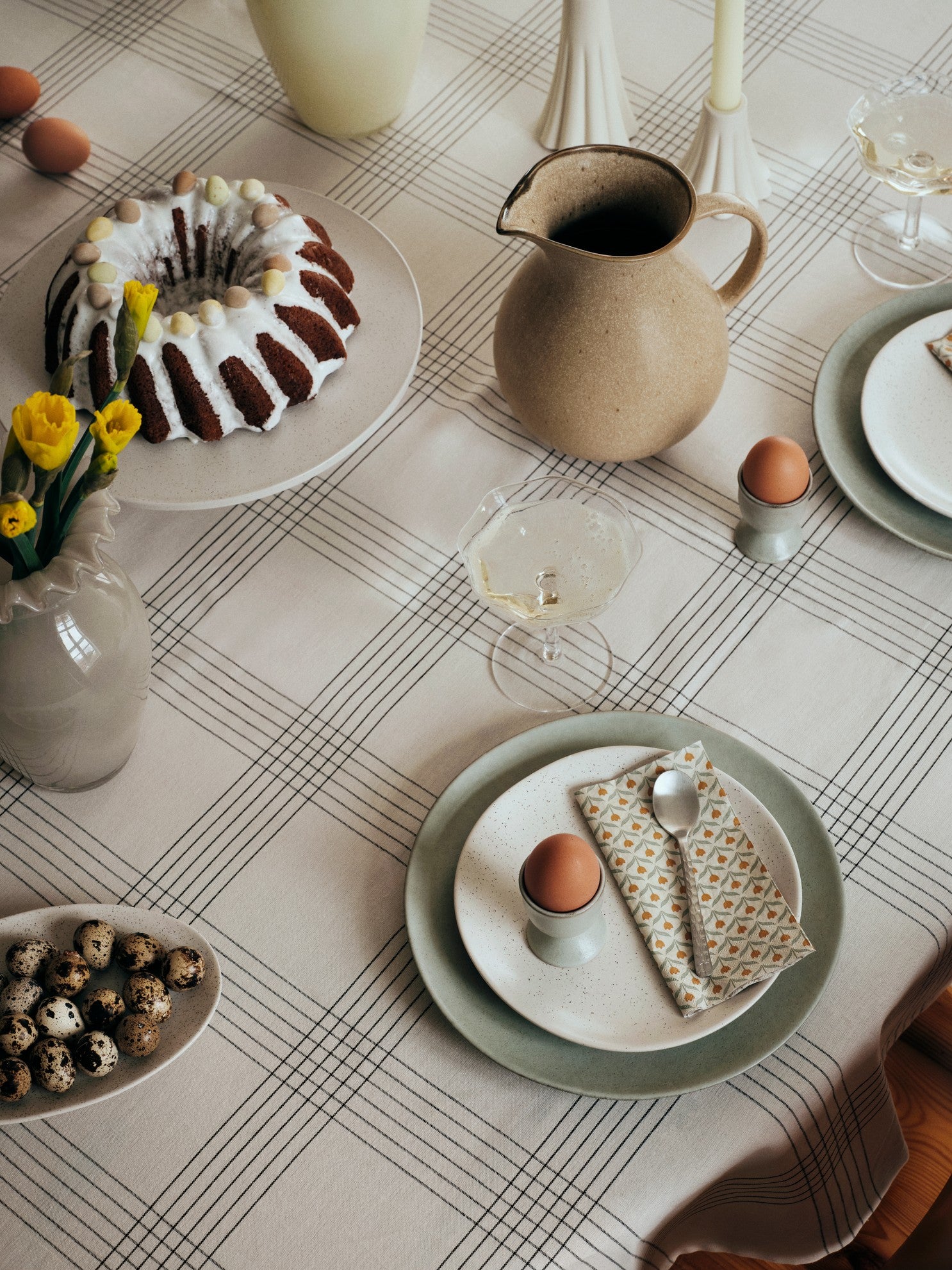 Easter table setting with cake, eggs, and decorative items on a checkered tablecloth.