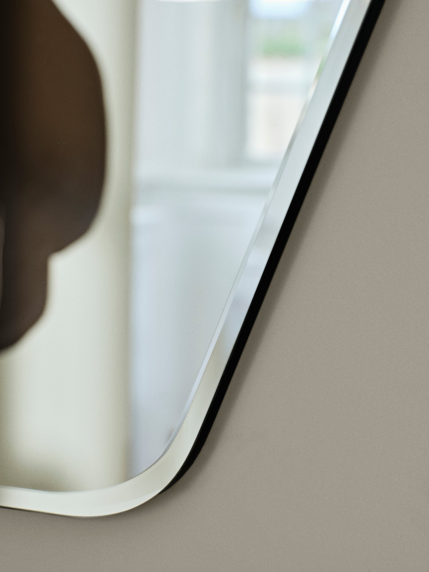 Close-up of a curved bevelled edge mirror with a black edge on a neutral background.