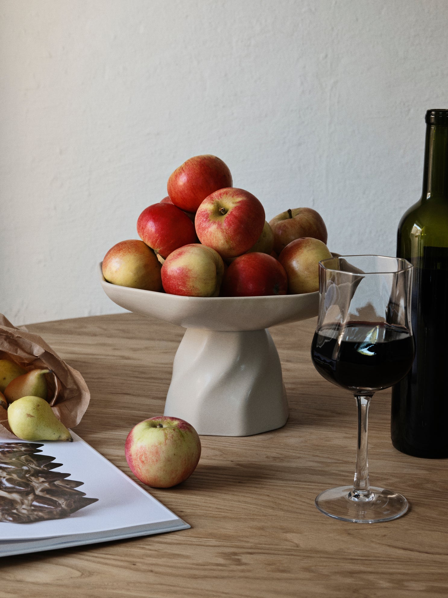 Bowl of apples on a wooden table with a glass of red wine and a bottle.
