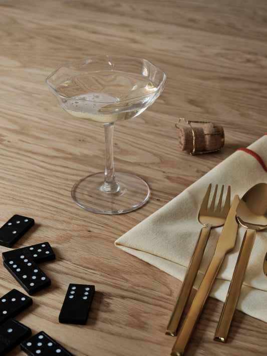 Glass with a drink, gold cutlery, and dominoes on a wooden table.