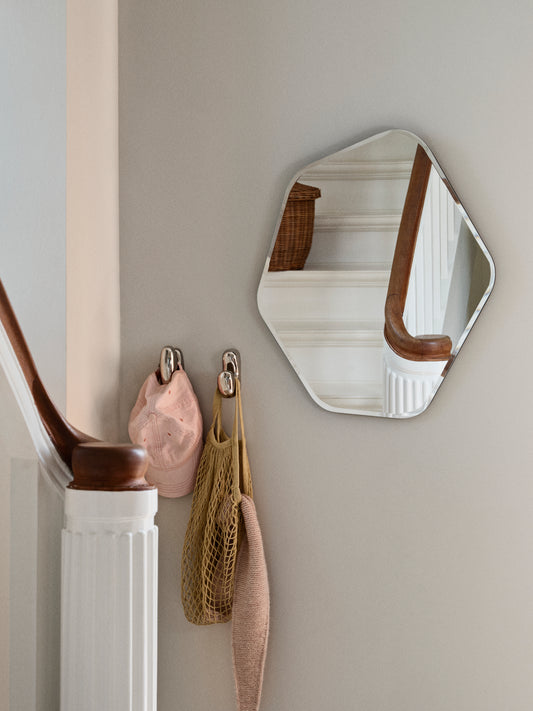 Hexagonal mirror with wooden frame on a wall above hooks with bags