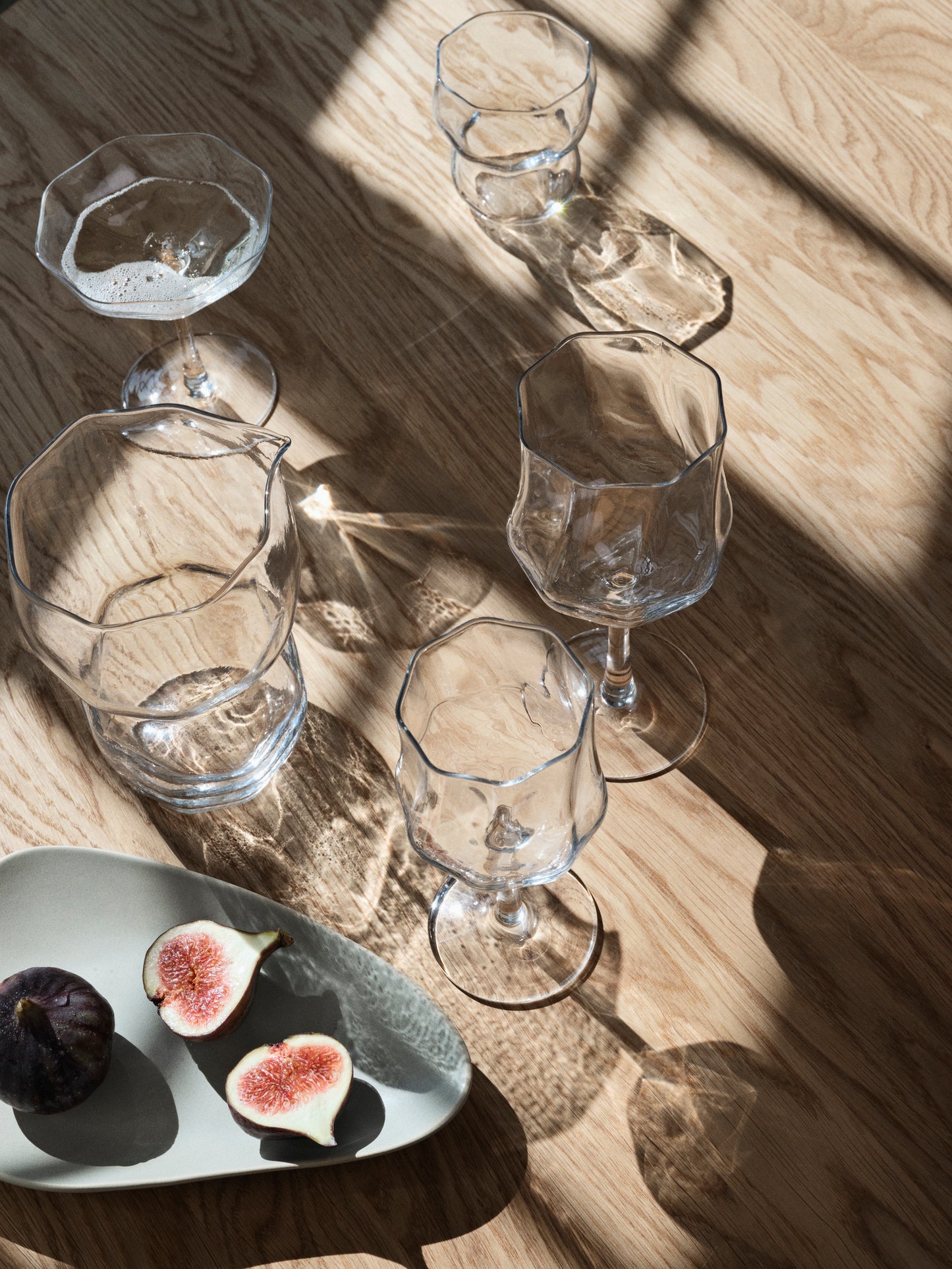 Clear glassware on a wooden surface with figs on a plate.