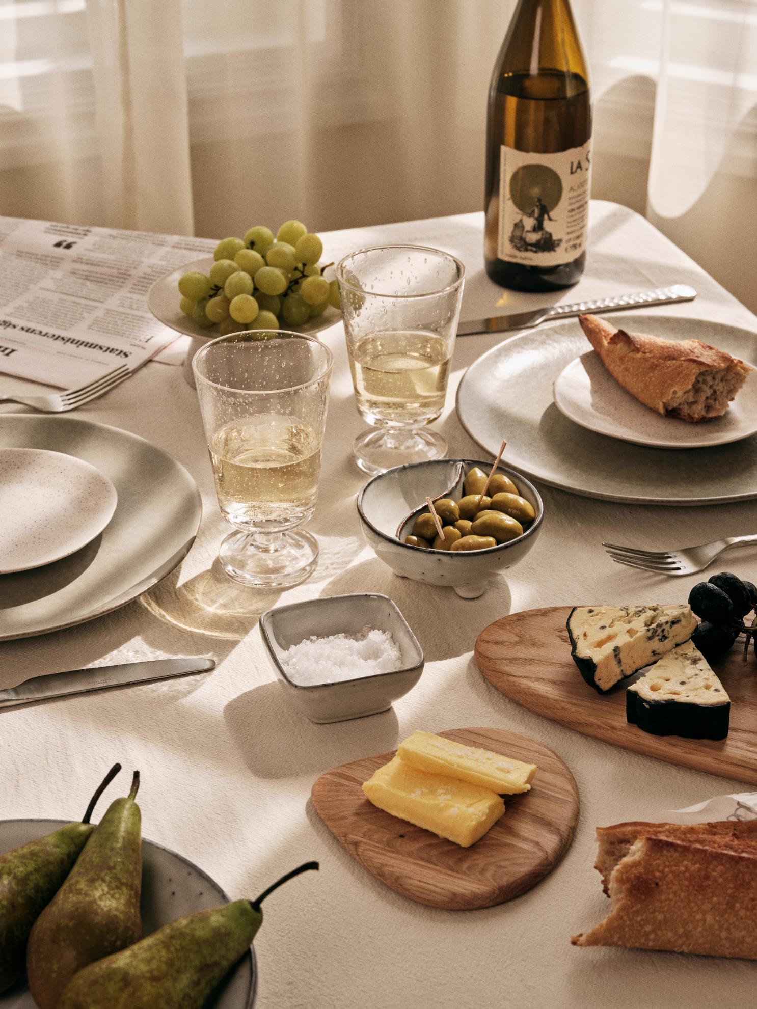 Beautifully laid table, natural cloth, cheese, olives, glassware and ceramics.