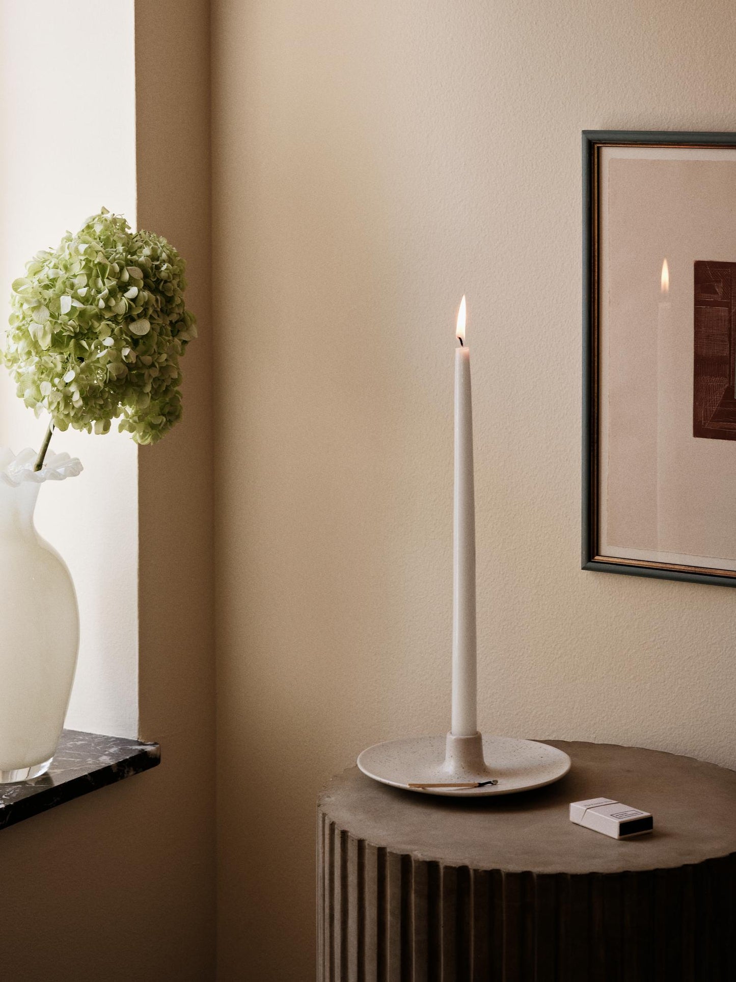 Ceramic wide candle holder with a tall elegant candle, against a pale pink background.